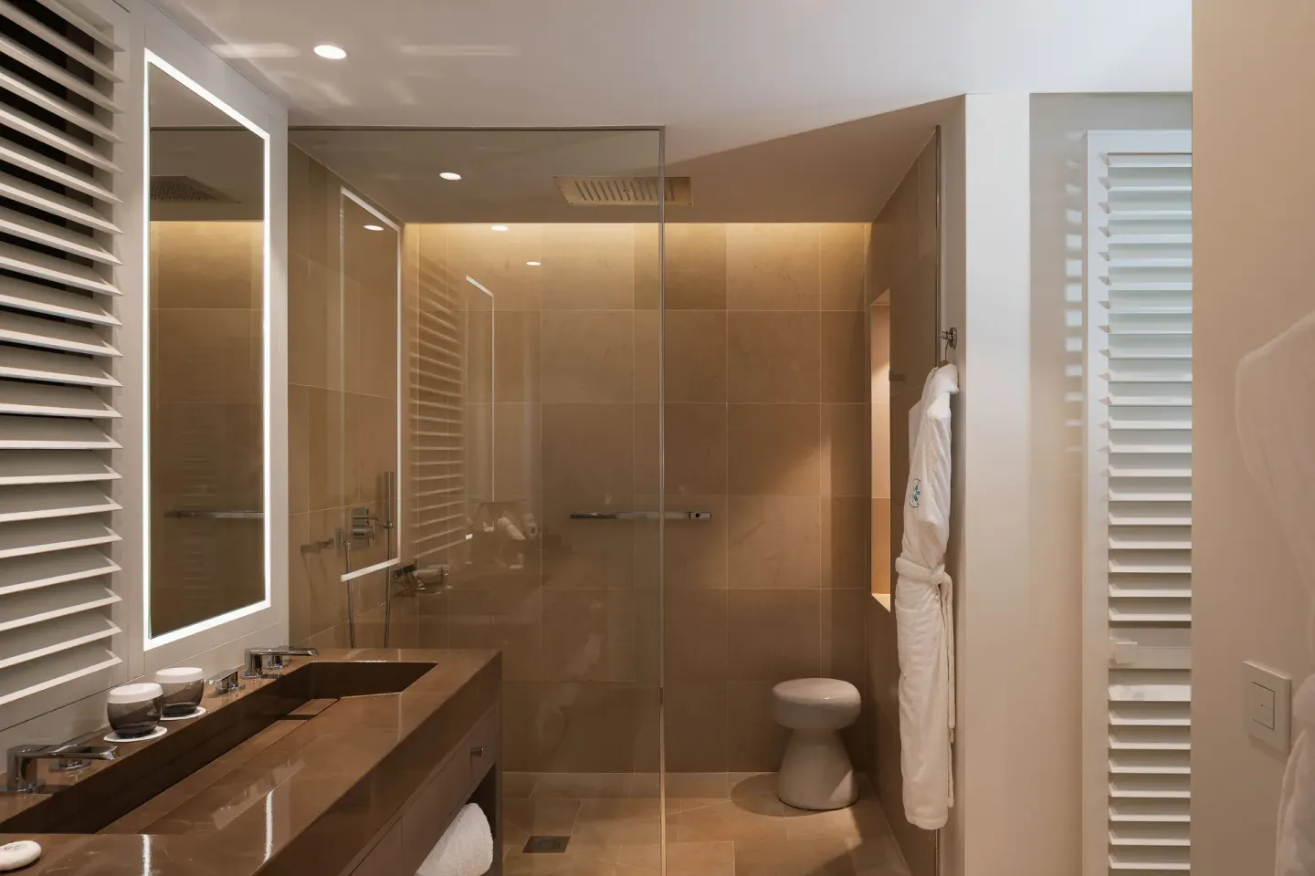 Bathroom with glass shower, vanity, and robe at Le Barthélemy Hotel & Spa.