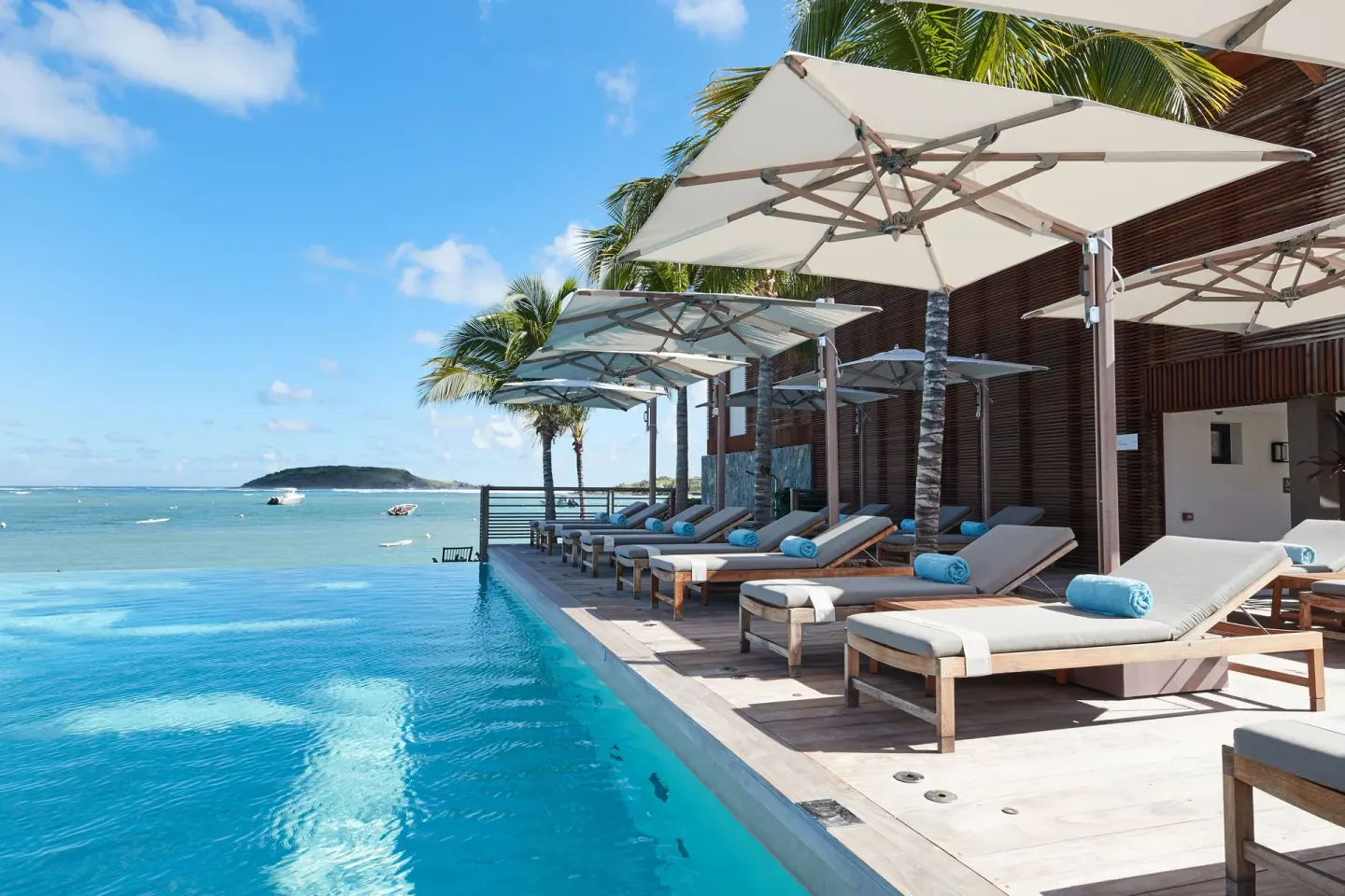 Infinity pool edge with shaded loungers and ocean beyond at Le Barthélemy Hotel & Spa.