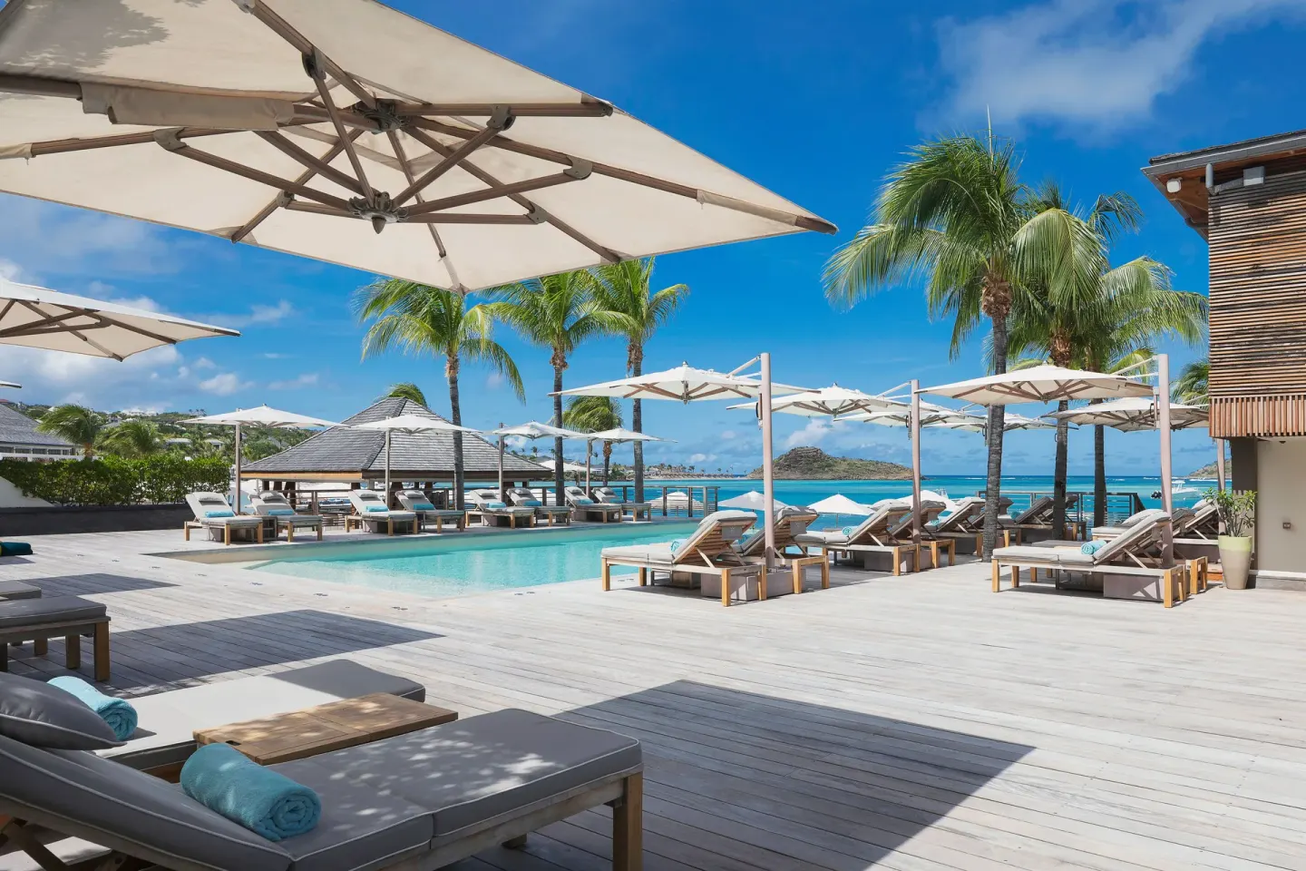 Pool deck with loungers, umbrellas and palms by the sea at Le Barthélemy Hotel & Spa.