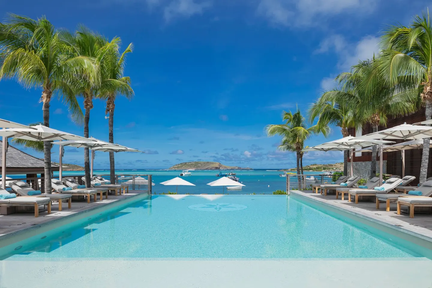 Resort pool framed by palms, loungers and turquoise bay at Le Barthélemy Hotel & Spa.