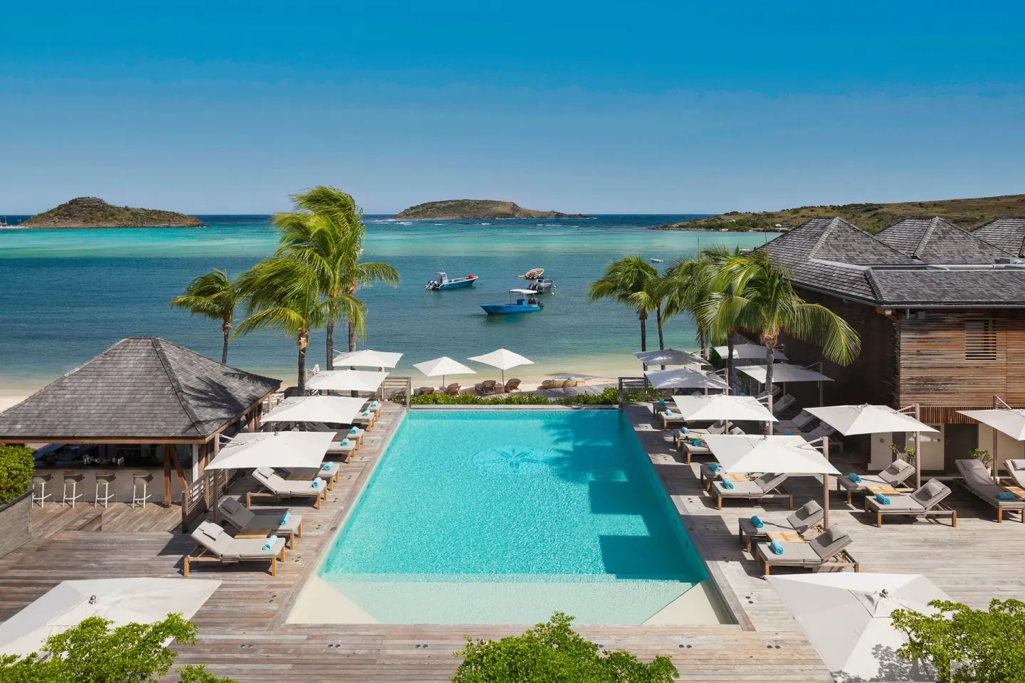 Elevated view of the pool, loungers, palms and lagoon at Le Barthélemy Hotel & Spa.