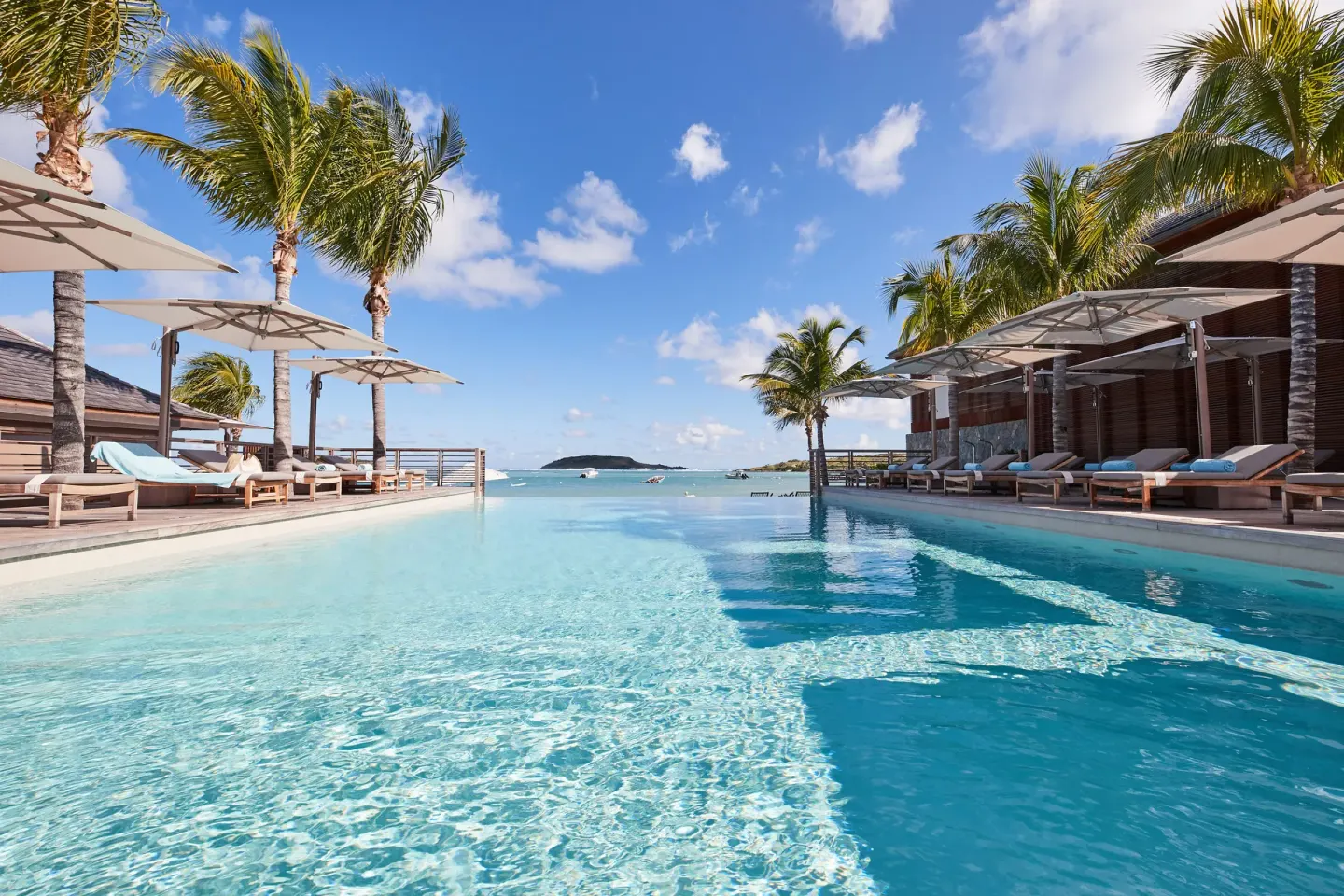 Low view across the pool toward palms, loungers and sea at Le Barthélemy Hotel & Spa.