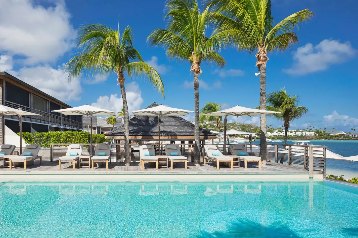Poolside loungers under umbrellas and palms at Le Barthélemy Hotel & Spa.