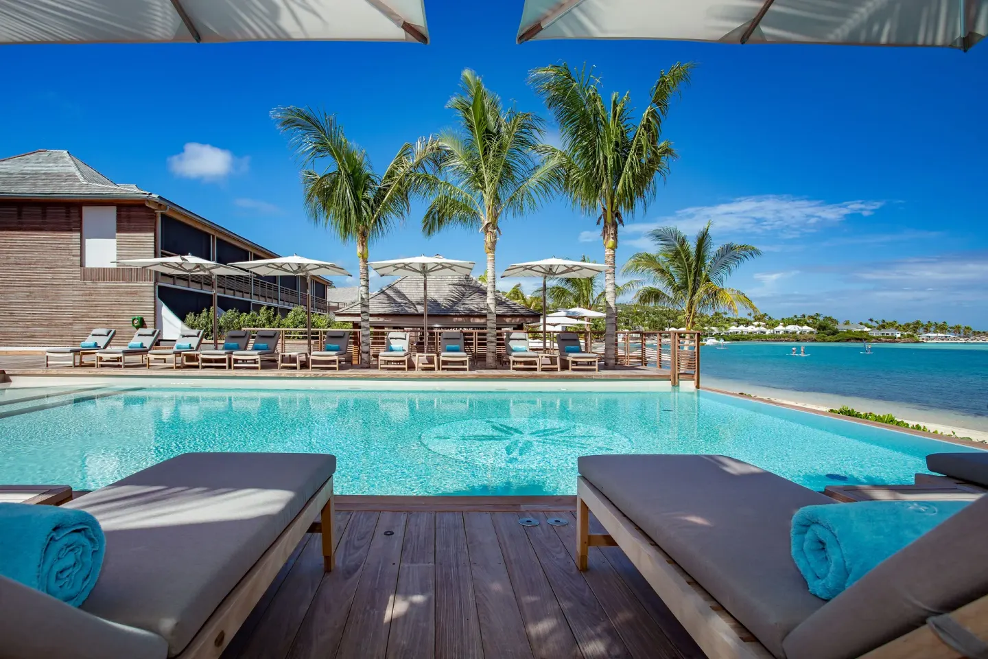 Resort pool with loungers, palms, and lagoon views at Le Barthélemy Hotel & Spa.