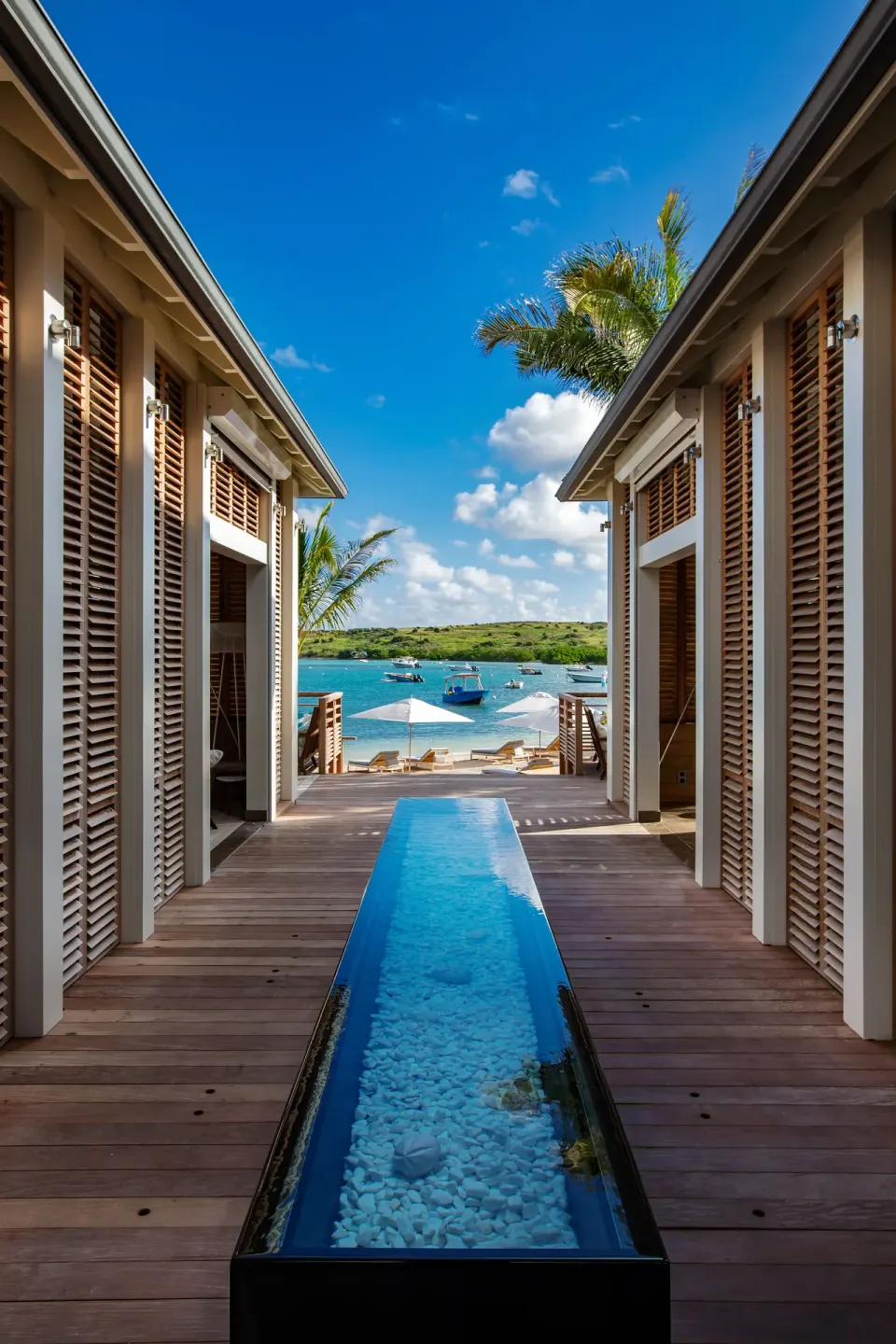 Wooden resort walkway with a narrow water feature and lagoon beyond at Le Barthélemy Hotel & Spa.