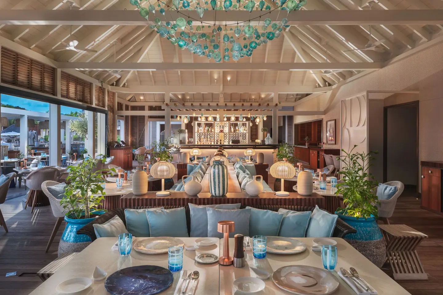 Open dining room with bar, set tables, and blue glass chandelier at Le Barthélemy Hotel & Spa.