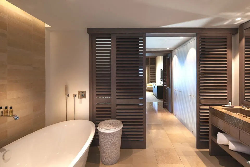 Bathroom in Le Duplex Océan Plage at Le Barthélemy Hotel & Spa with freestanding tub and louvered doors.