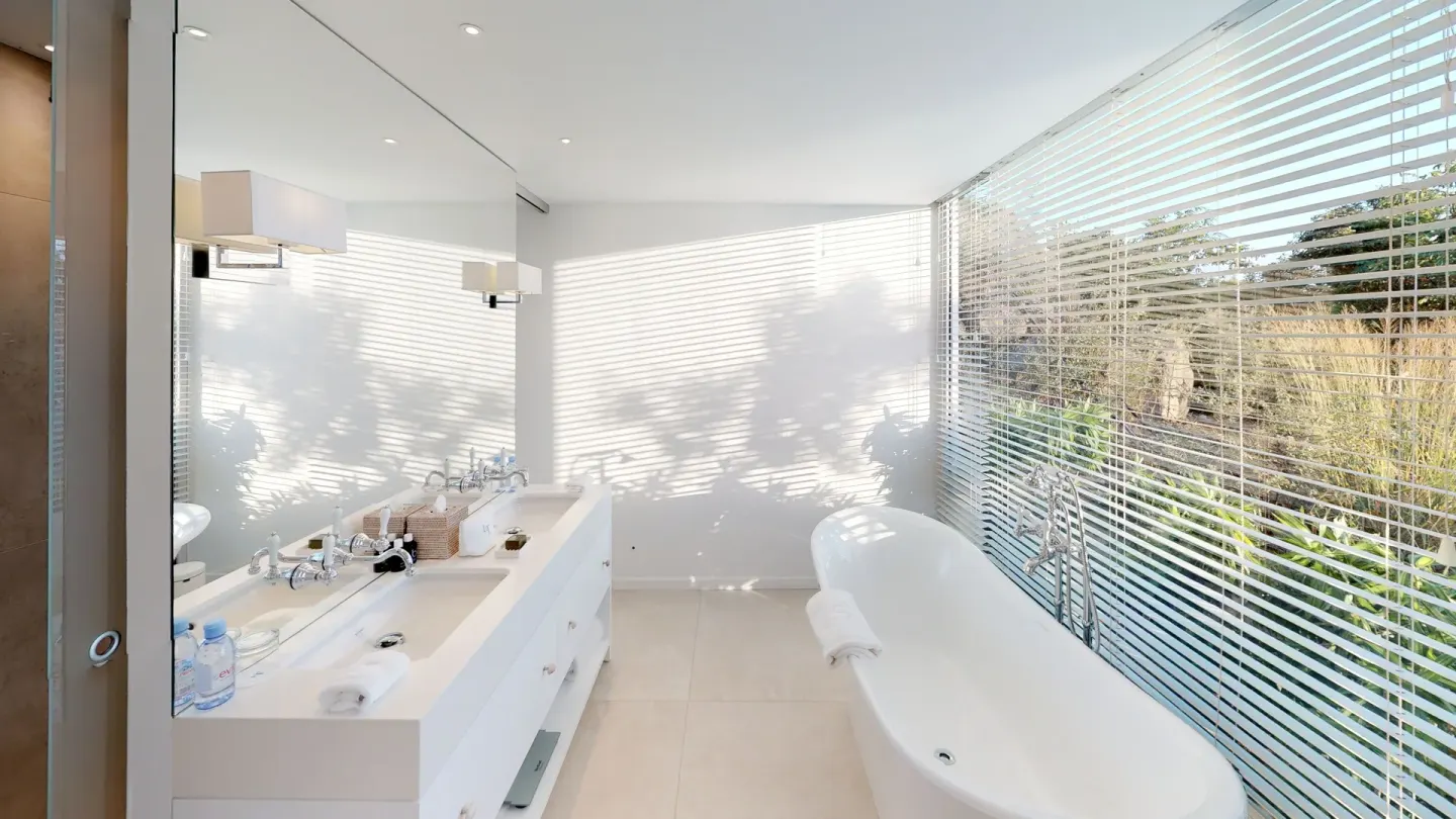 White bathroom with double vanity, freestanding tub and garden blinds at Le Toiny Hôtel & Beach Club.
