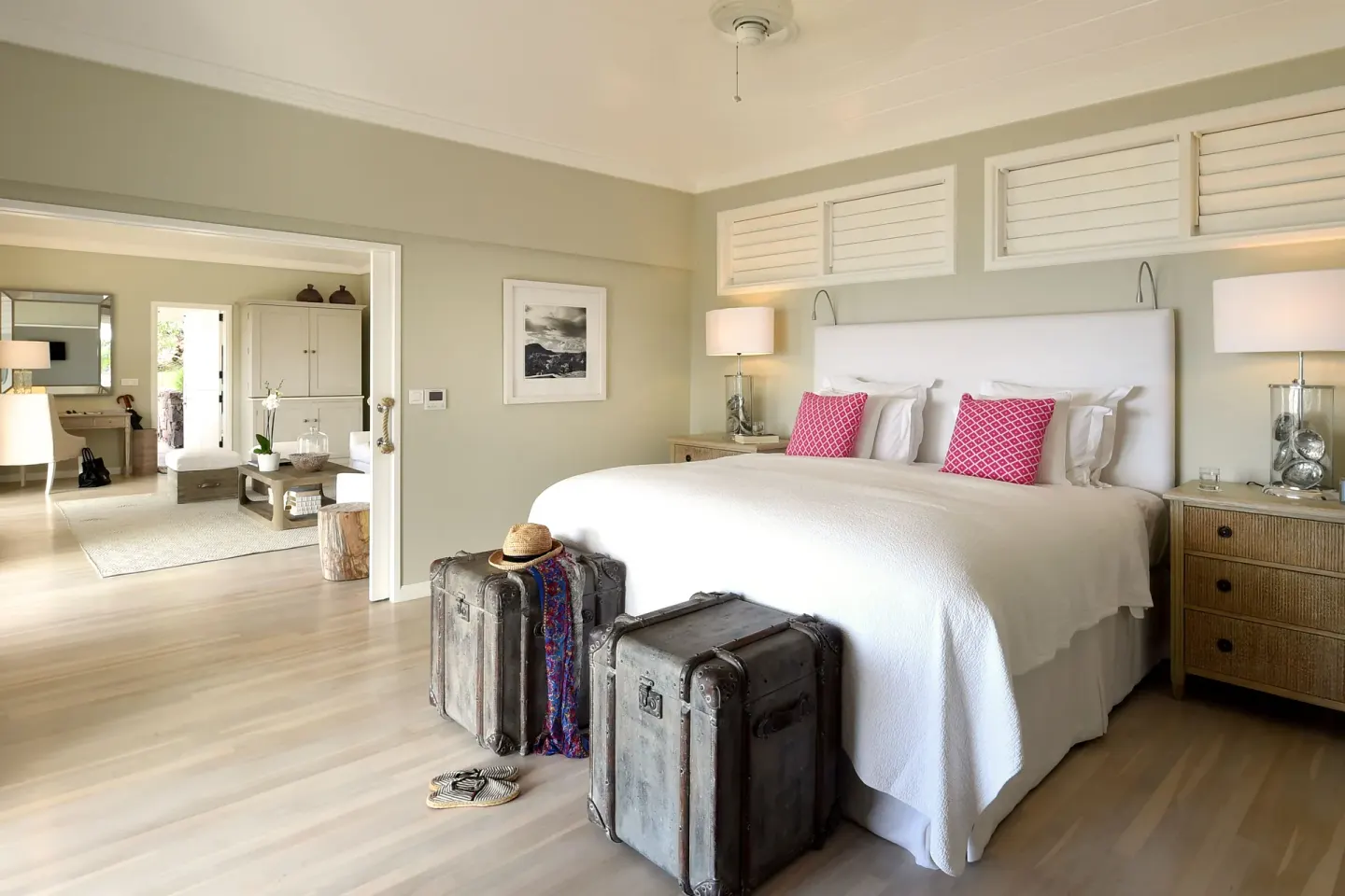 Guest bedroom with a white king bed, vintage trunks, and sitting area at Le Toiny Hôtel & Beach Club.
