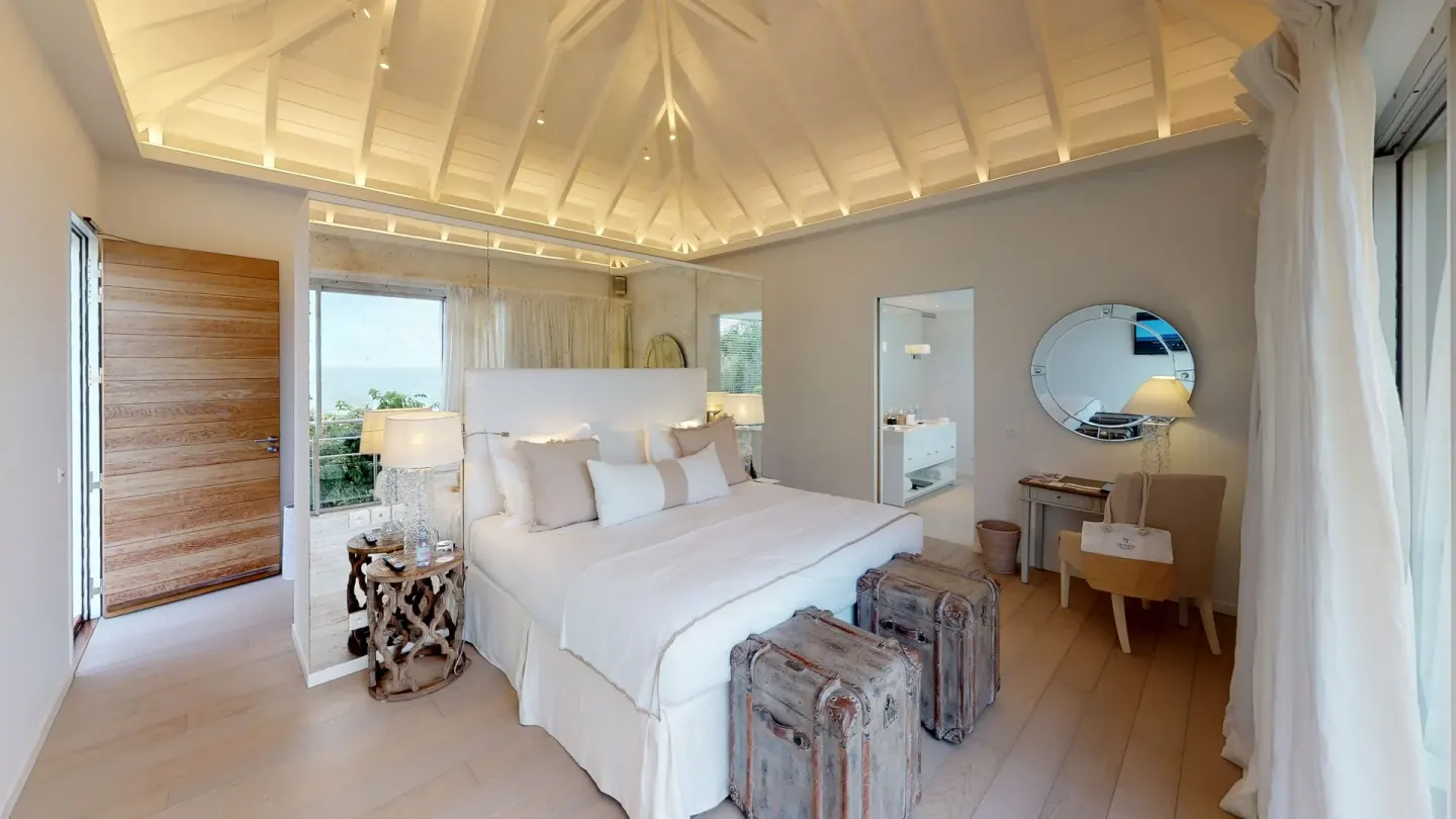 Guest room with a white king bed, luggage, desk, and vaulted ceiling at Le Toiny Hôtel & Beach Club.