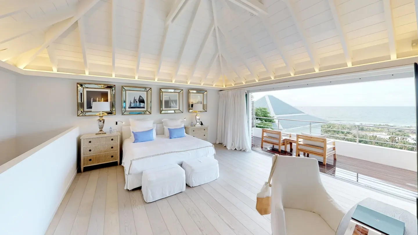 Guest room with twin beds, vaulted ceiling, terrace seating, and sea view at Le Toiny Hôtel & Beach Club.