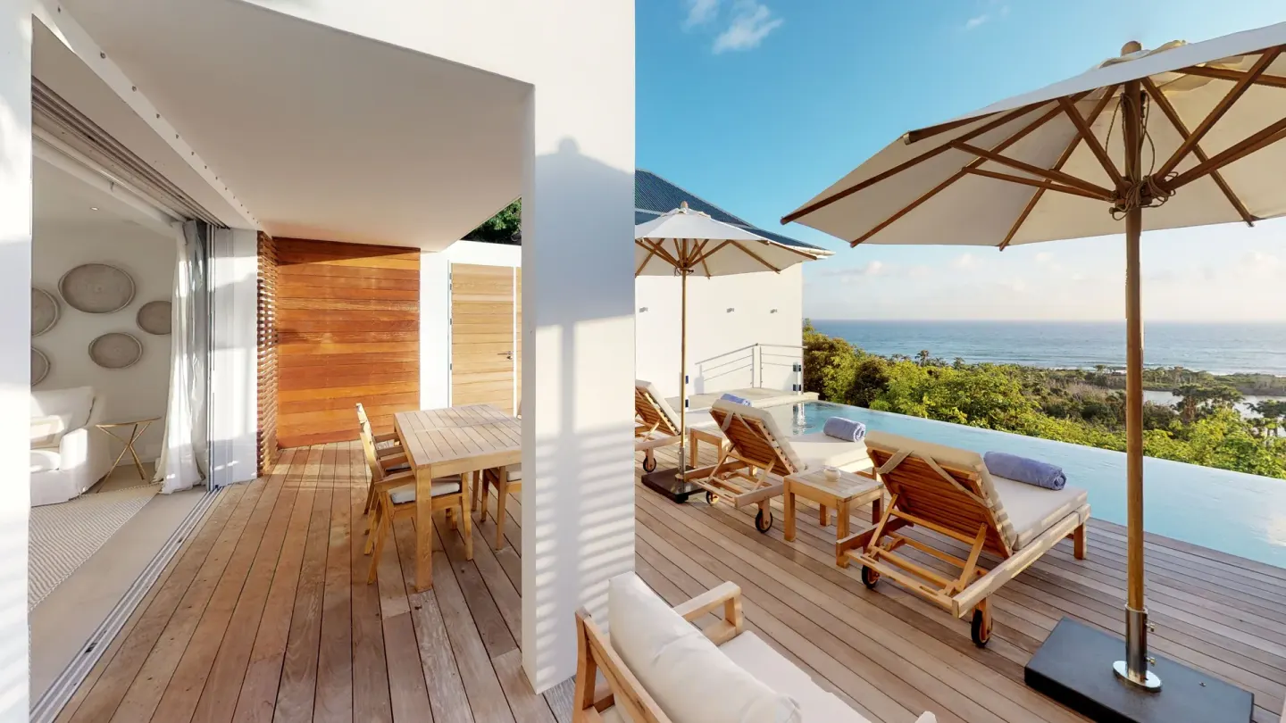 Ocean-facing villa deck with loungers, umbrellas and indoor seating at Le Toiny Hôtel & Beach Club.