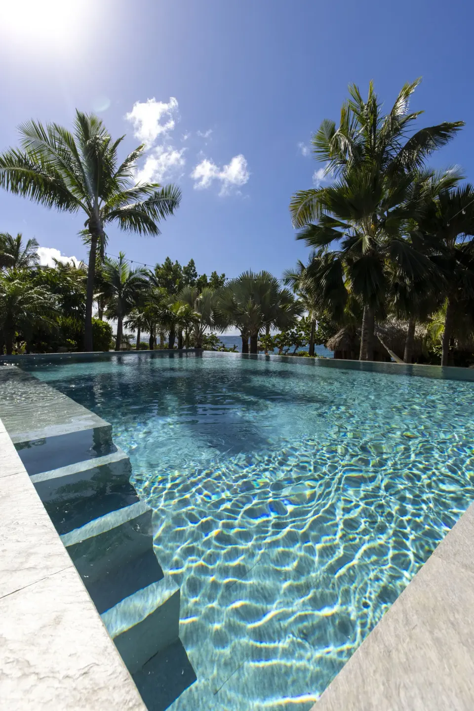 Pool steps and palms under a blue sky at Le Toiny Hôtel & Beach Club.