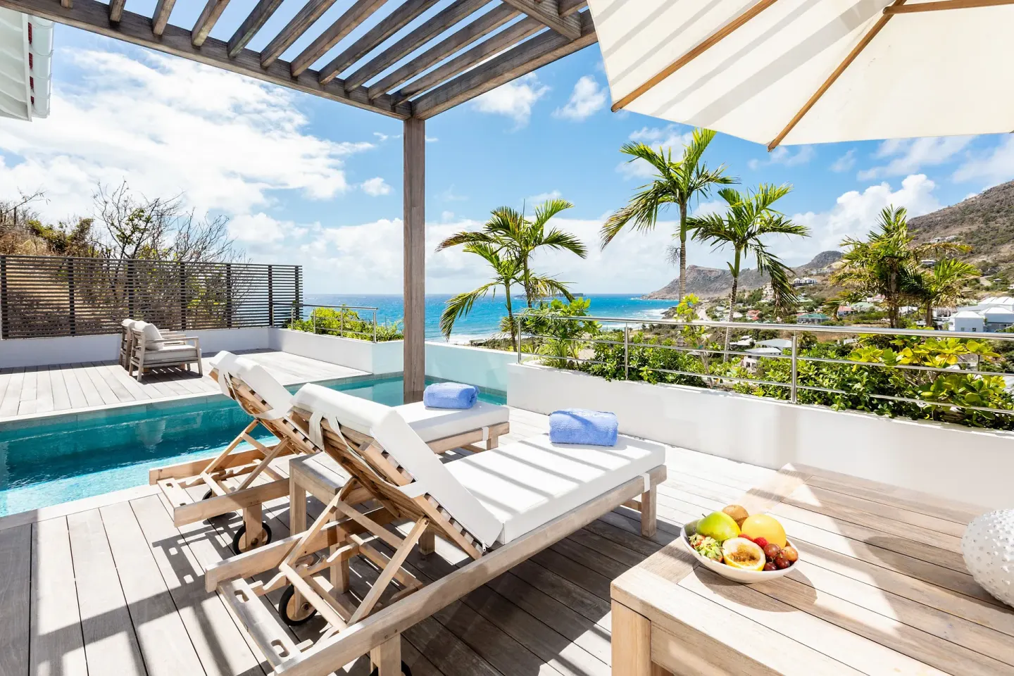 Sunlit pool terrace with loungers, palms and ocean view at Le Toiny Hôtel & Beach Club.
