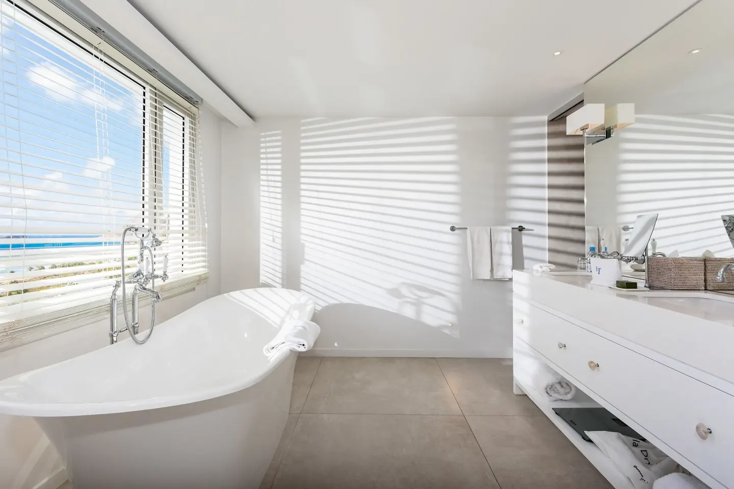Sunlit bathroom with freestanding tub and ocean glimpse at Le Toiny Hôtel & Beach Club.