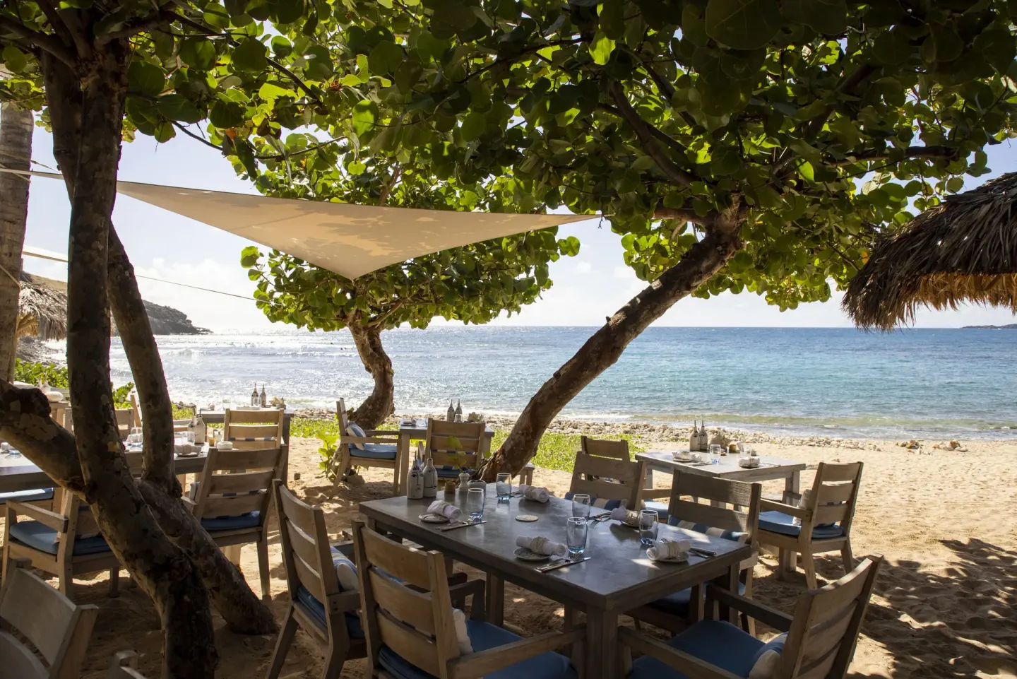 Beachfront dining tables beneath trees at the Beach Club at Le Toiny Hôtel & Beach Club.