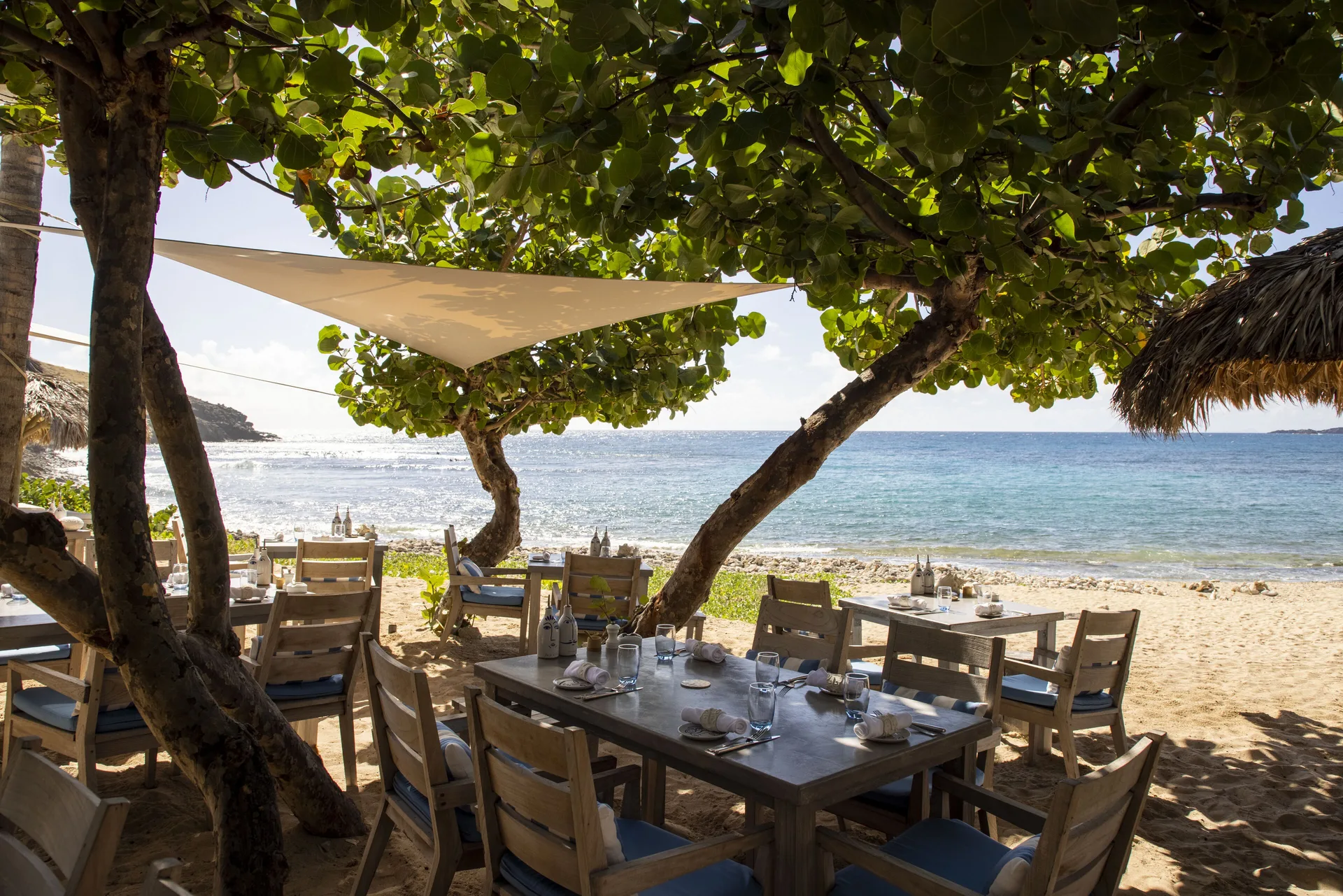 Beachfront dining tables beneath trees at the Beach Club at Le Toiny Hôtel & Beach Club.