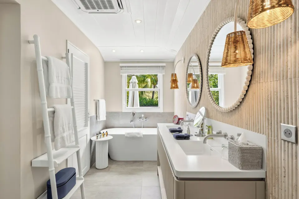 Junior Suite bathroom at Le Toiny Hôtel & Beach Club with double vanity, tub, and window greenery.