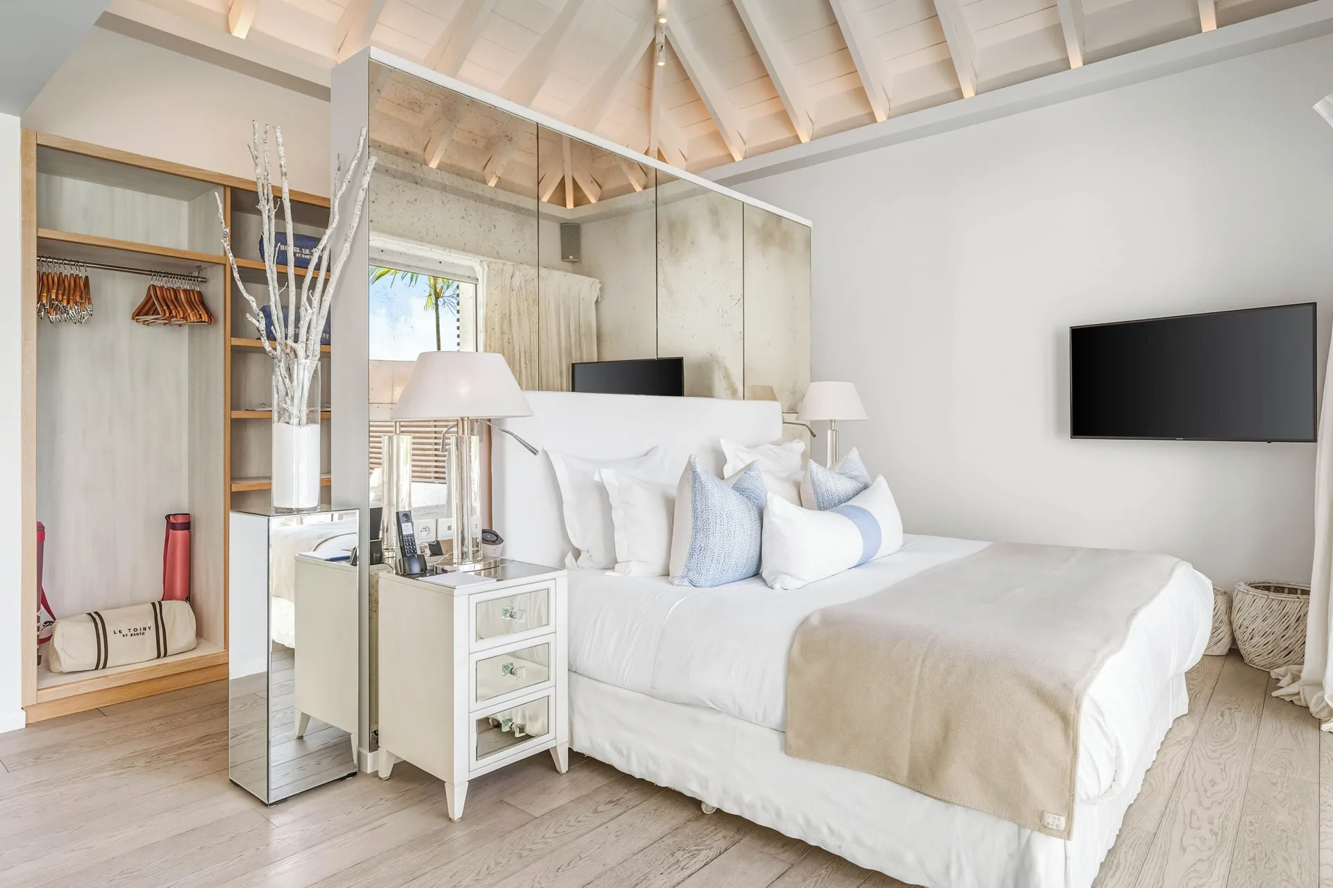 Spirit Suite king bed with mirrored wall, open closet, and TV at Le Toiny Hôtel & Beach Club.