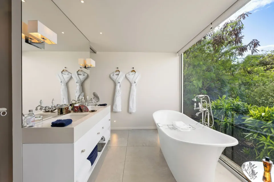 Bright villa bathroom at Le Toiny Hôtel & Beach Club with a freestanding tub beside garden-view glass.