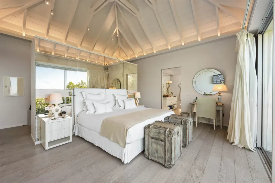 Bedroom with king bed, mirrored headboard, and luggage trunks at Le Toiny Hôtel & Beach Club.