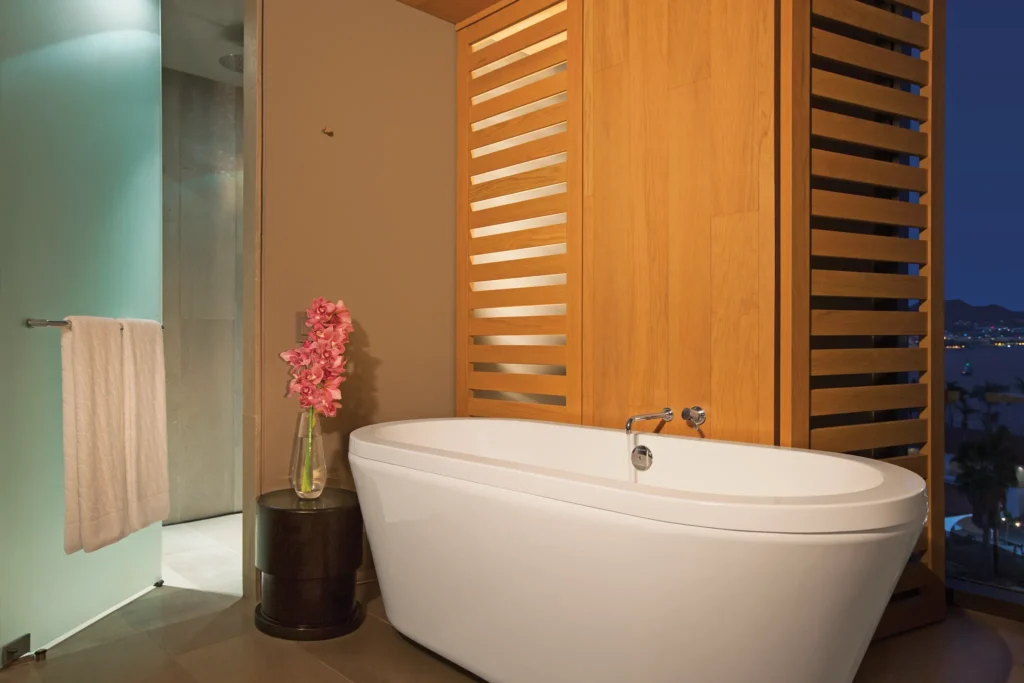 Freestanding soaking tub with nighttime ocean views in the Xhale Club Master One Bedroom Suite at Breathless Cabo San Lucas.