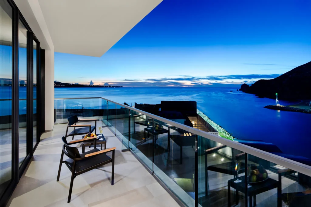Nighttime oceanfront balcony with illuminated coastline views from the Xhale Club Master One Bedroom Suite at Breathless Cabo San Lucas.