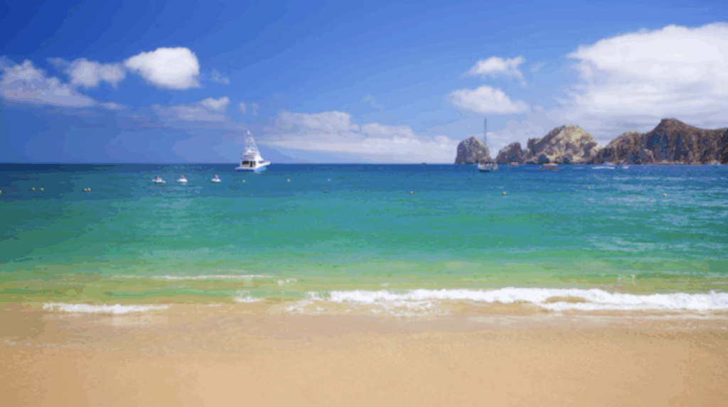 Scenic view of Cabo San Lucas Bay with turquoise water, golden sand, and Land’s End rock formations in the distance.
