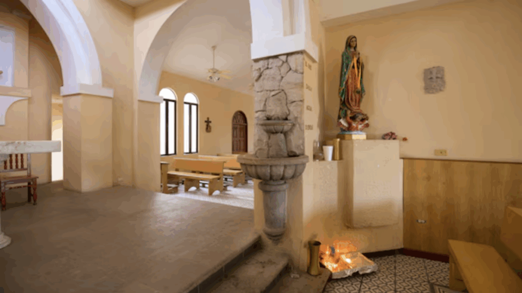 Interior of the Church of Saint Luke in Cabo San Lucas with arches, wooden benches, and religious statues.