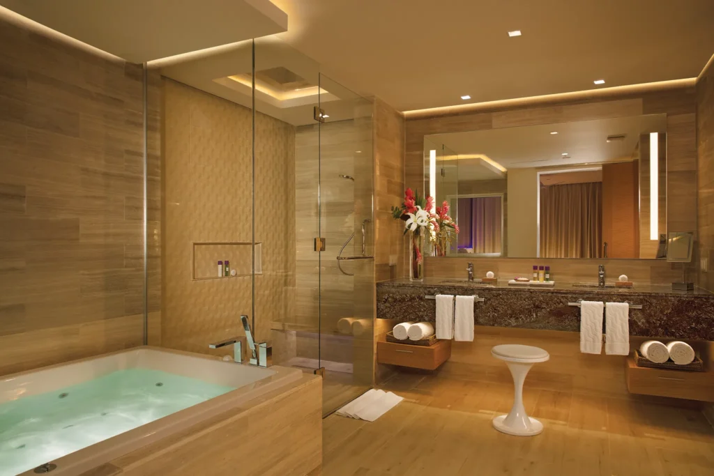 Xhale Club Master Suite Swim-Up bathroom at Breathless Montego Bay featuring a large soaking tub, rainfall shower, and elegant double-sink vanity in warm modern décor.