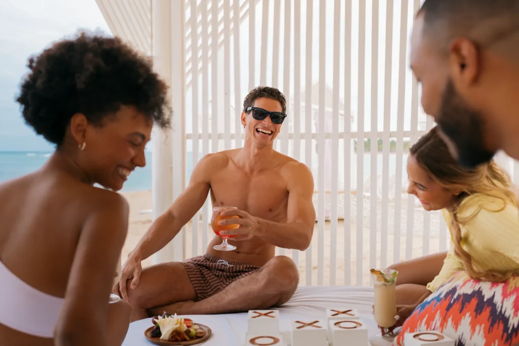 Friends relaxing inside a shaded beach cabana at Breathless Punta Cana with cocktails and ocean views.