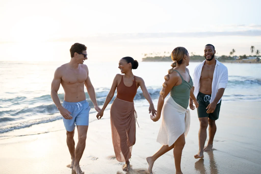 Group of friends walking along the shoreline at Breathless Punta Cana during a sunny beach day.