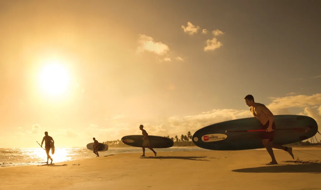 Guests carrying paddleboards along the beach at sunset at Breathless Punta Cana.
