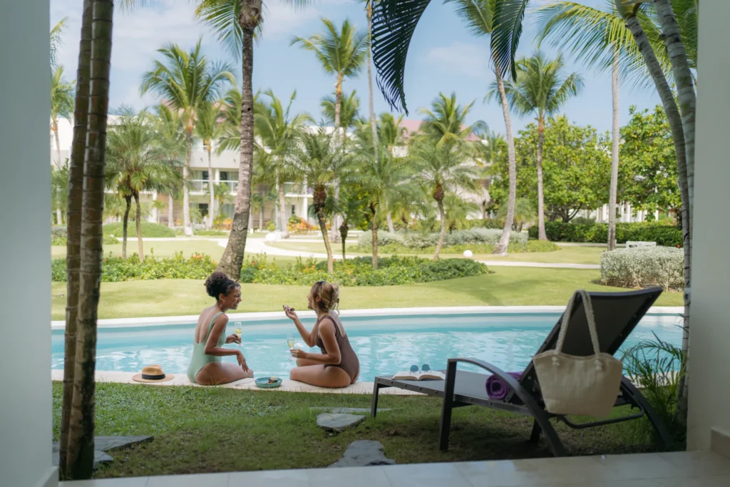 Friends relaxing together poolside at Breathless Punta Cana surrounded by tropical landscaping.