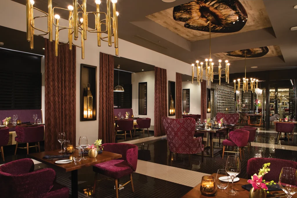 Elegant interior of Coquette, the French fine-dining restaurant at Breathless Riviera Cancun with gold chandeliers and rich décor.