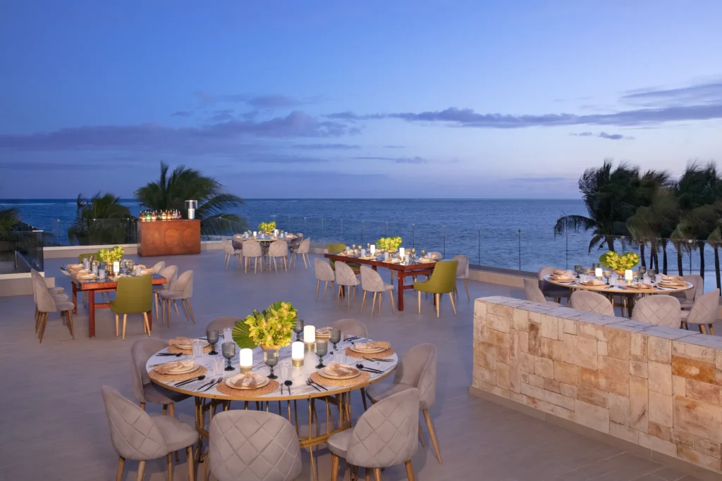 Oceanfront terrace banquet setup at Breathless Riviera Cancun featuring round tables, candles, floral arrangements, and sea views.