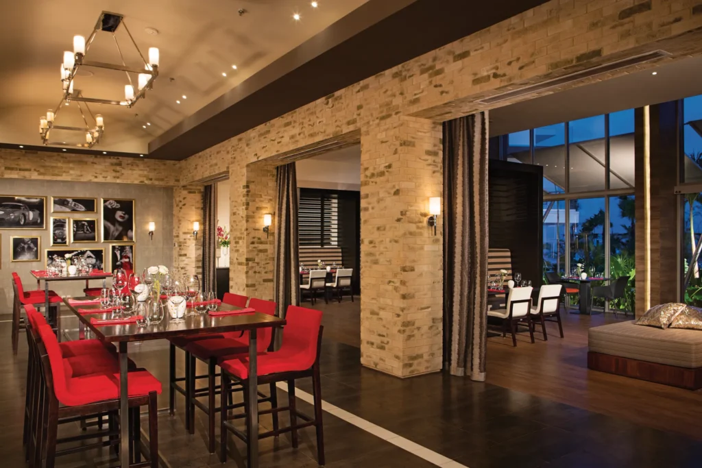 Interior of Spumante, the Italian restaurant at Breathless Riviera Cancun, featuring modern décor, red seating, and elegant dining tables.