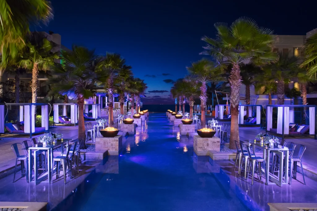 Nighttime cocktail reception along the Xcelerate Pool at Breathless Riviera Cancun, featuring fire bowls, tall tables, and cabanas.