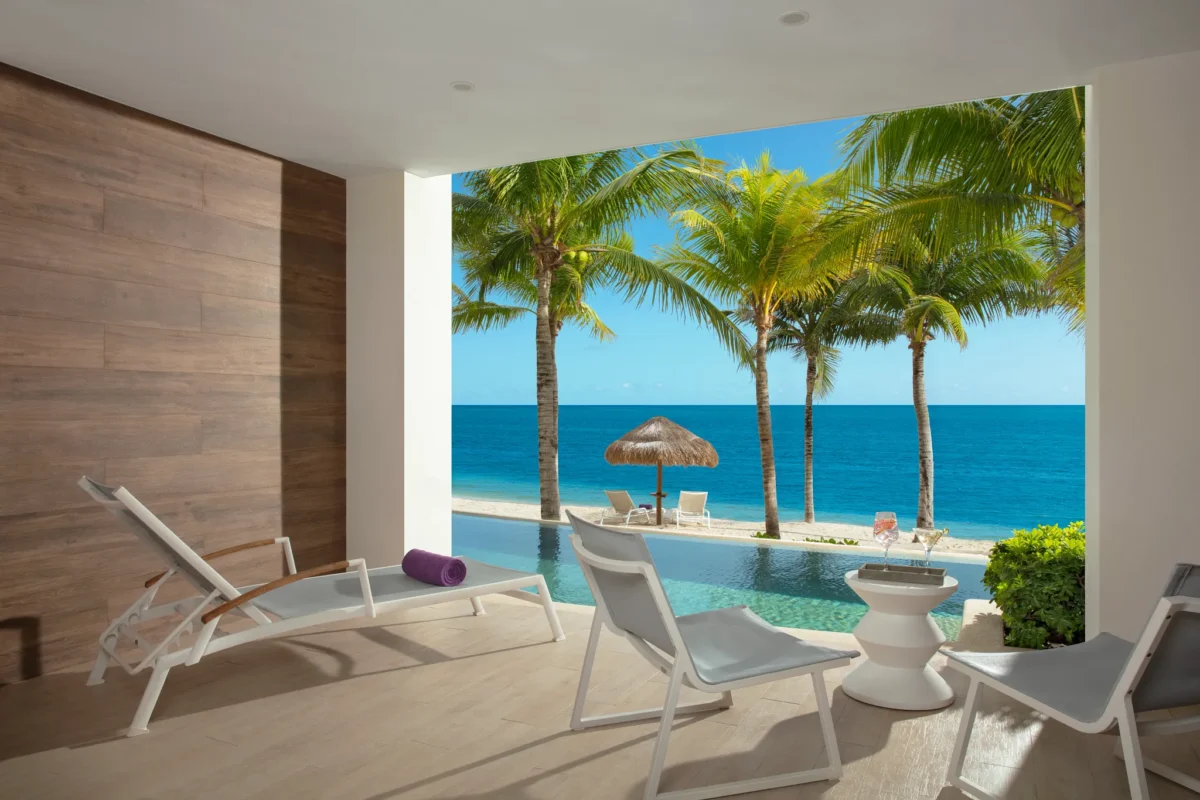 Oceanfront swim-out pool view from the Xhale Club Junior Suite Swim Out Ocean Front at Breathless Riviera Cancun with palm trees and Caribbean Sea.