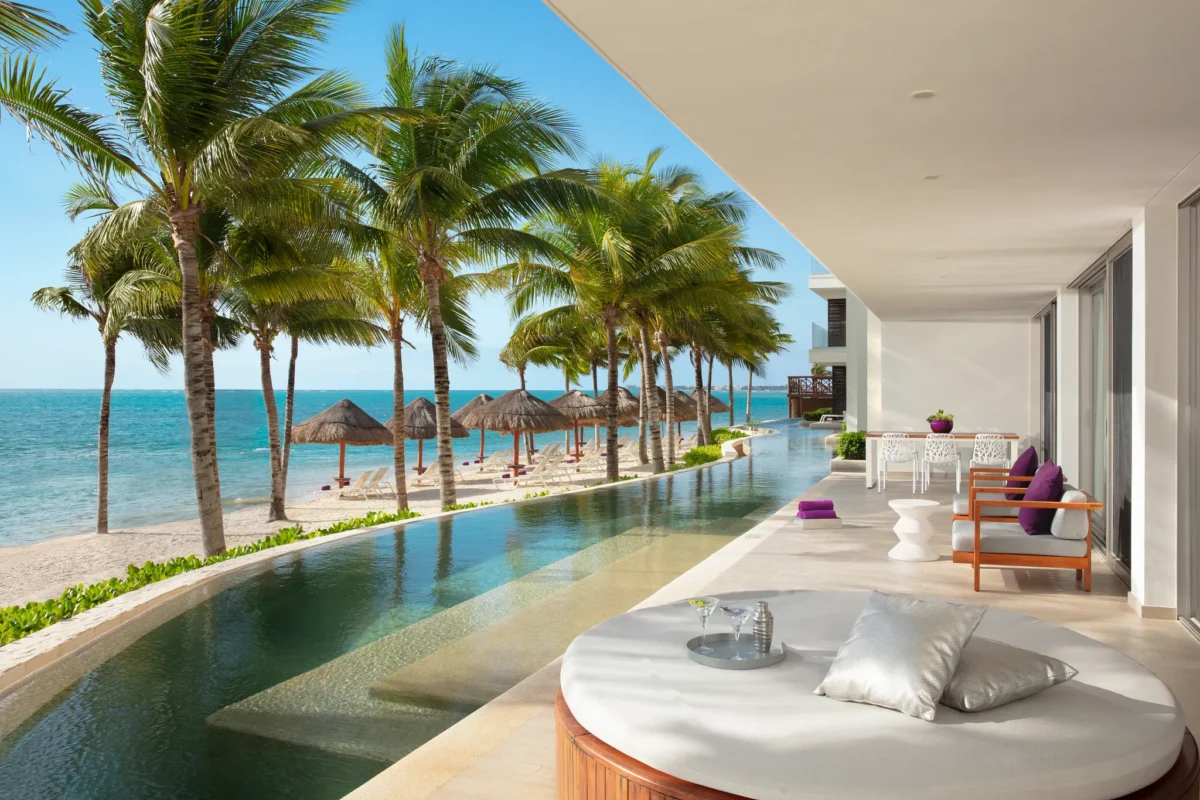 Ocean-front swim-out terrace at the Xhale Club Presidential Suite at Breathless Riviera Cancun featuring a private pool, lounge seating, palm trees, and panoramic Caribbean Sea views.