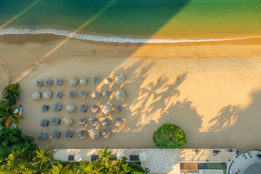 Overhead view of beachfront palapas and golden sand at Dreams Acapulco Resort & Spa along Acapulco Bay.