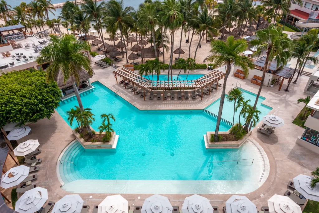 Aerial view of family pool with lounge chairs and palm trees at Dreams Aventuras Riviera Maya.