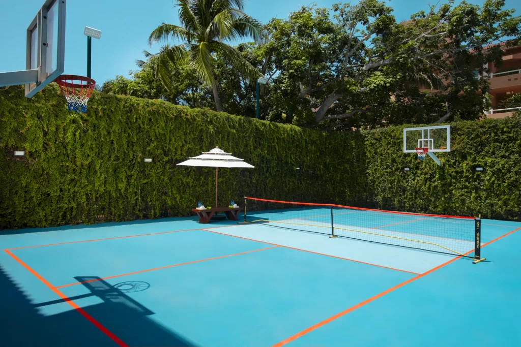 Outdoor pickleball court with basketball hoops at Dreams Aventuras Riviera Maya, surrounded by lush greenery and tropical landscaping.