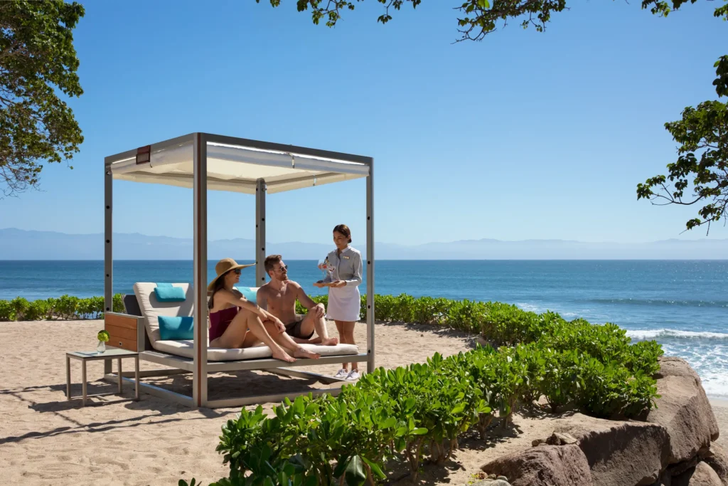 Couple relaxing in a private beach cabana with ocean views and drink service at Dreams Bahia Mita.