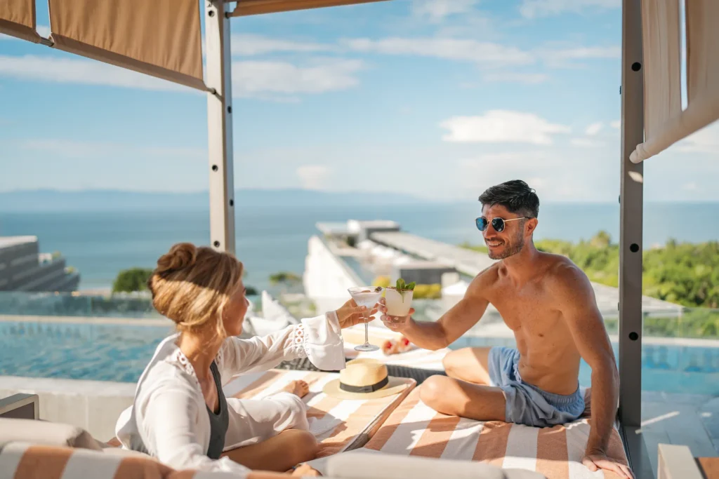 Couple toasting cocktails poolside with ocean views at Dreams Bahia Mita resort.