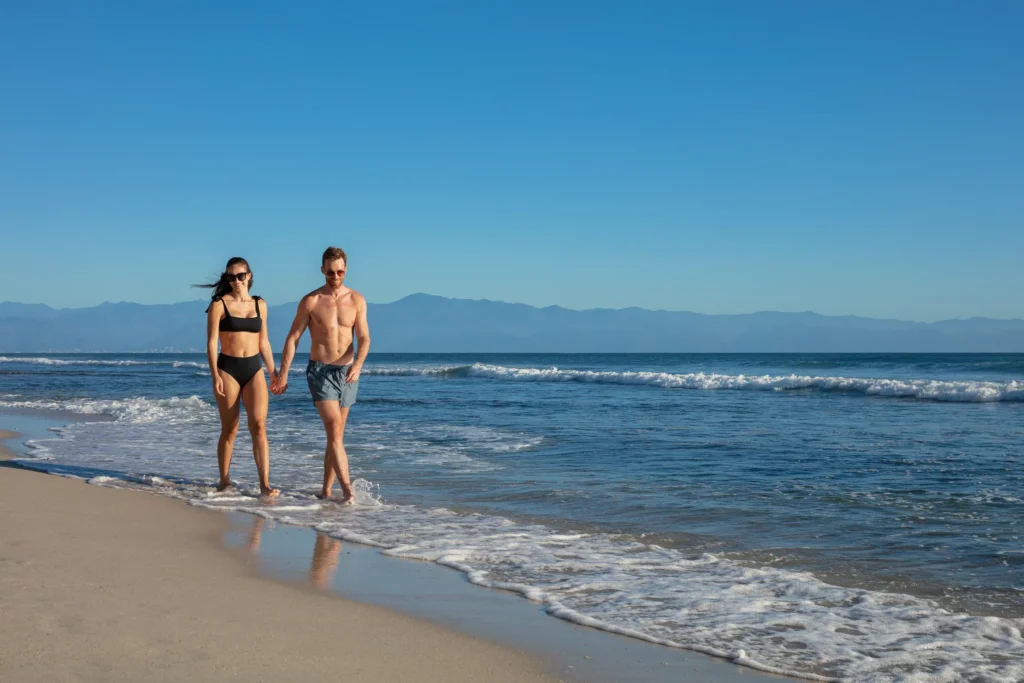 Couple walking hand in hand along the shoreline at Dreams Bahia Mita beach.