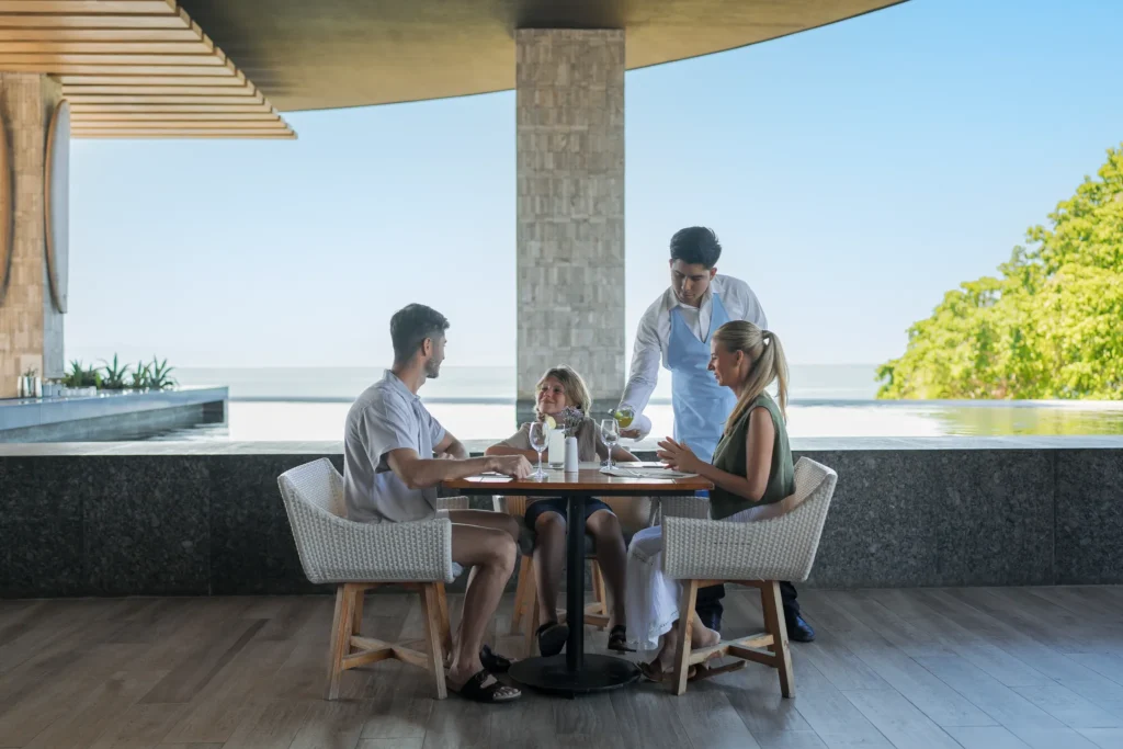 Family dining at restaurant with ocean view and server at Dreams Bahia Mita.