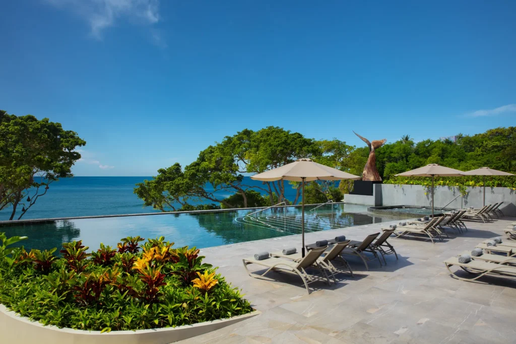 Infinity pool overlooking the ocean with lounge chairs and umbrellas at Dreams Bahia Mita.