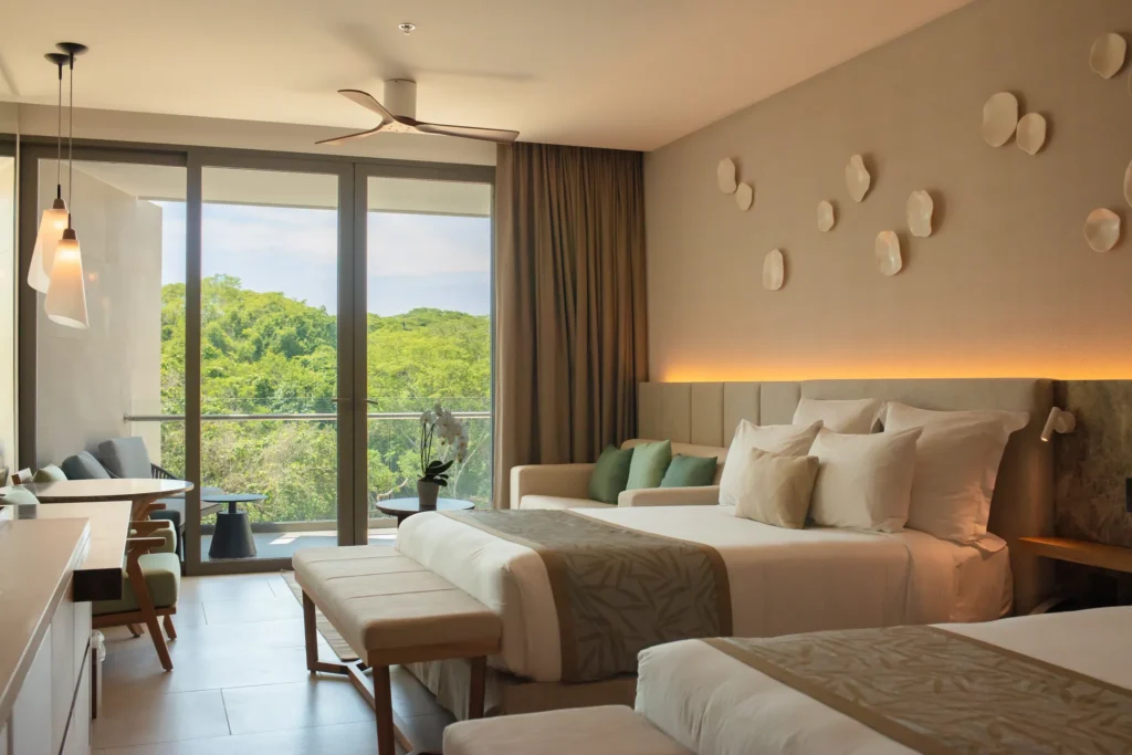 Junior Suite Tropical View with two queen beds and balcony at Dreams Bahia Mita Surf & Spa Resort overlooking lush greenery.