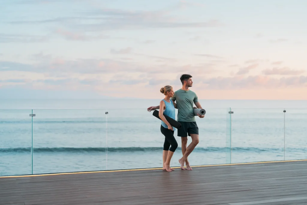 Couple walking barefoot with yoga mats along an oceanview deck at Dreams Bahia Mita.